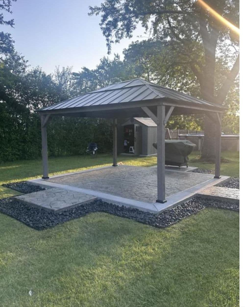 backyard gazebo with metal roof on stone patio, surrounded by gravel and grass in evening light