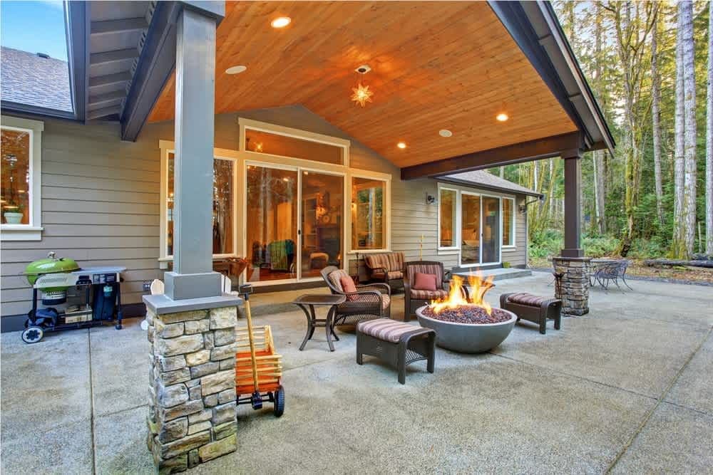 Modern outdoor living space with fire pit, seating area, and wooded backdrop. Ideal for gatherings.
