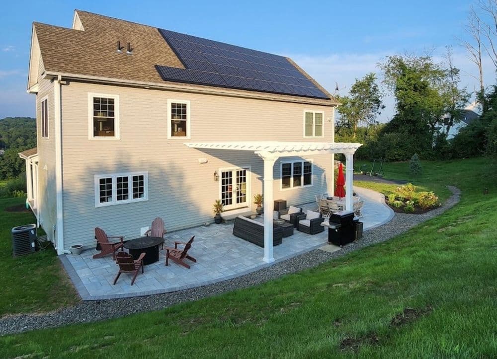 Modern home with solar panels, patio furniture, and landscaped yard in a serene setting.